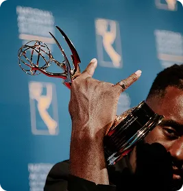 Close-up of a person holding a Emmy Award trophy near their face against a blue backdrop.